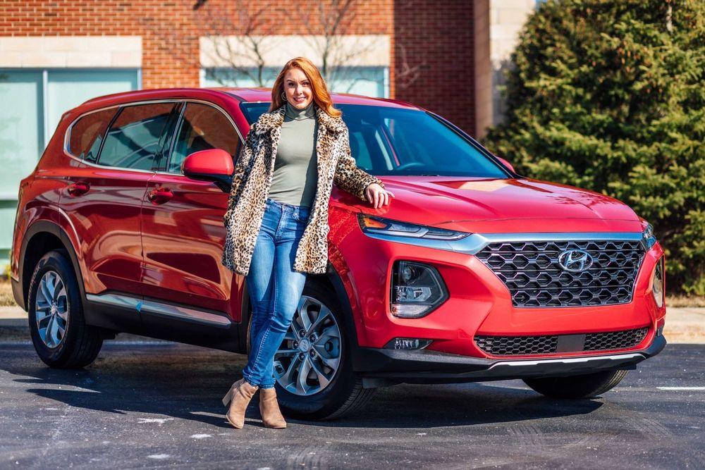 Woman with red hair standing next to a red Hyundai.
