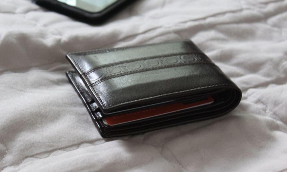 A black leather wallet on a bed.