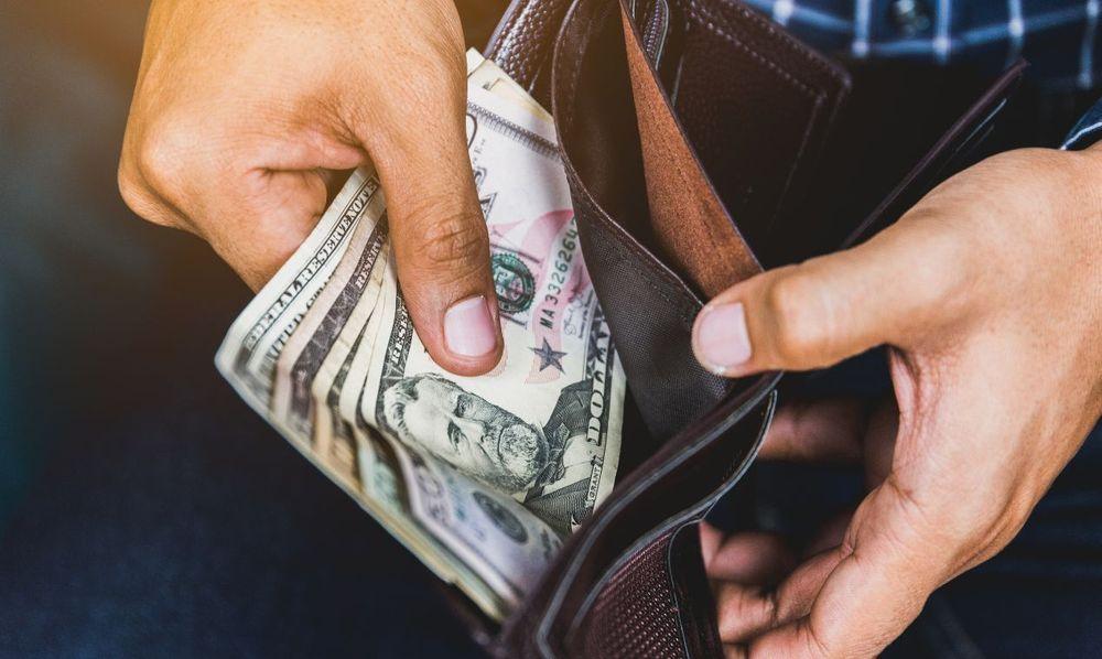 Person holding a brown leather wallet with money inside