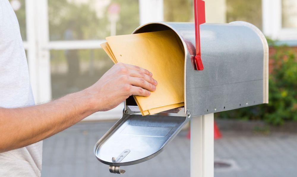 Person putting manilla envelopes inside of an open mailbox