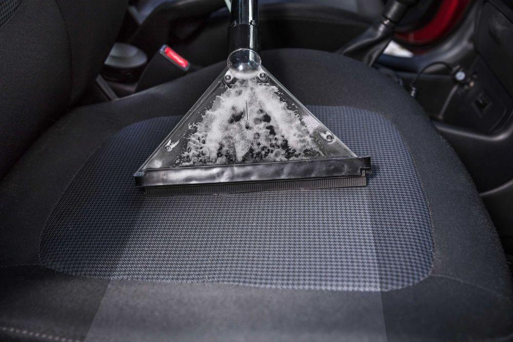 Person using a wet vacuum on cloth car interior.