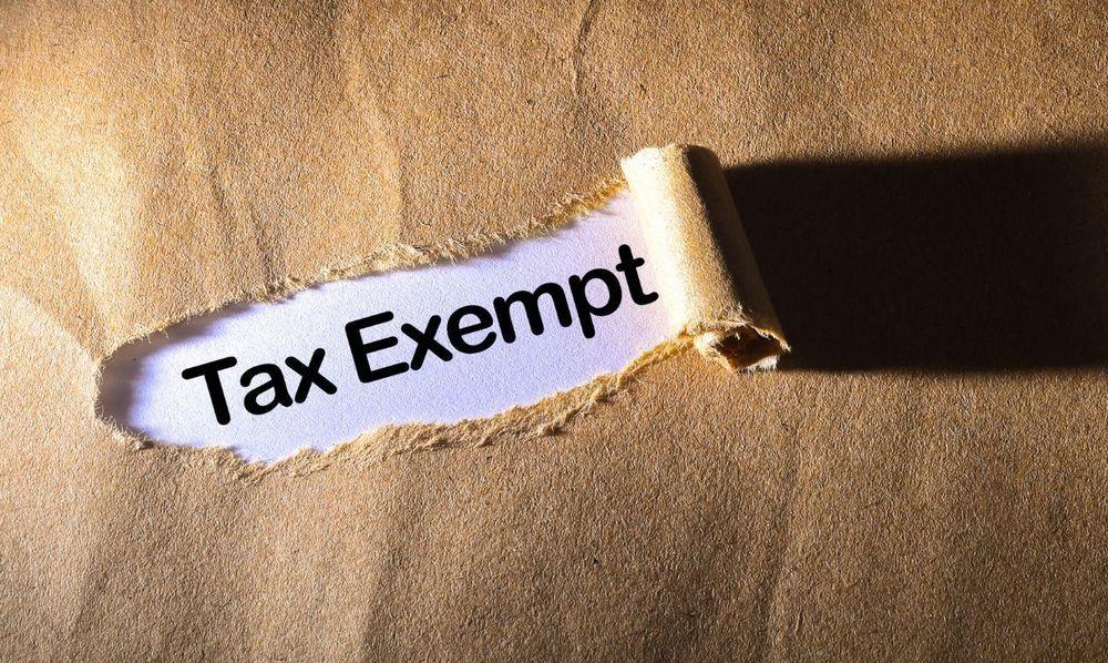 The word tax exempt on a white piece of paper under ripped, brown, construction paper