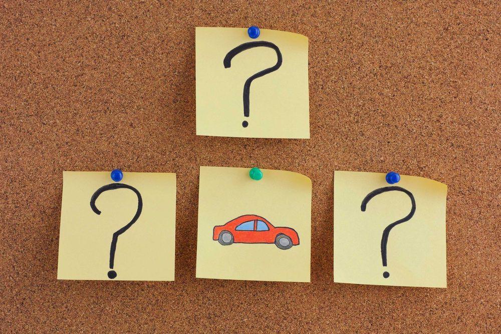Question marks and a car drawn on sticky notes and pinned to a cork board.