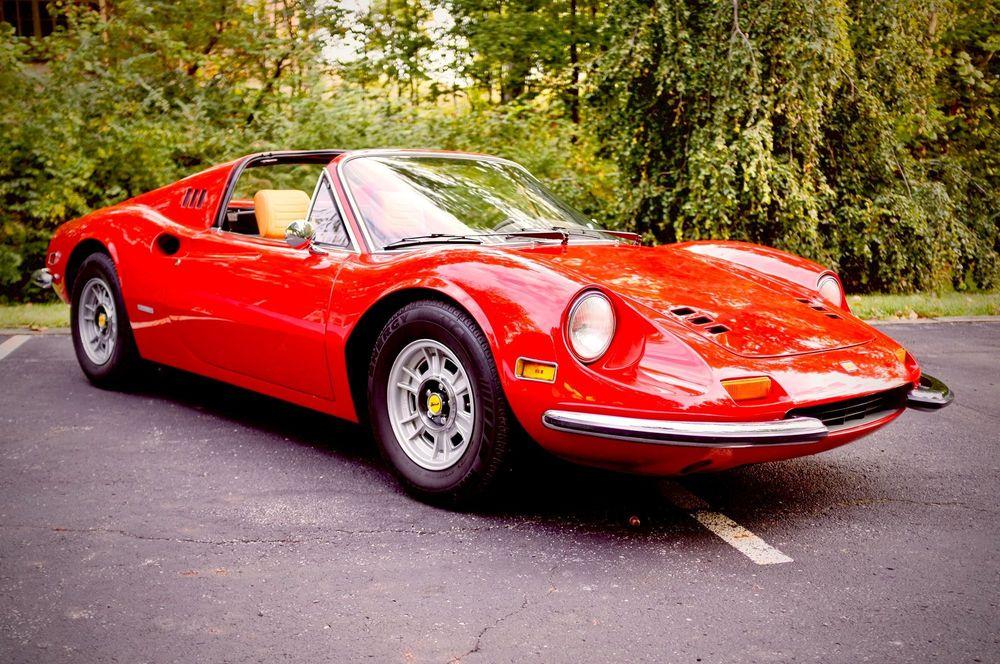 Red classic car in parking lot in front of greenery.