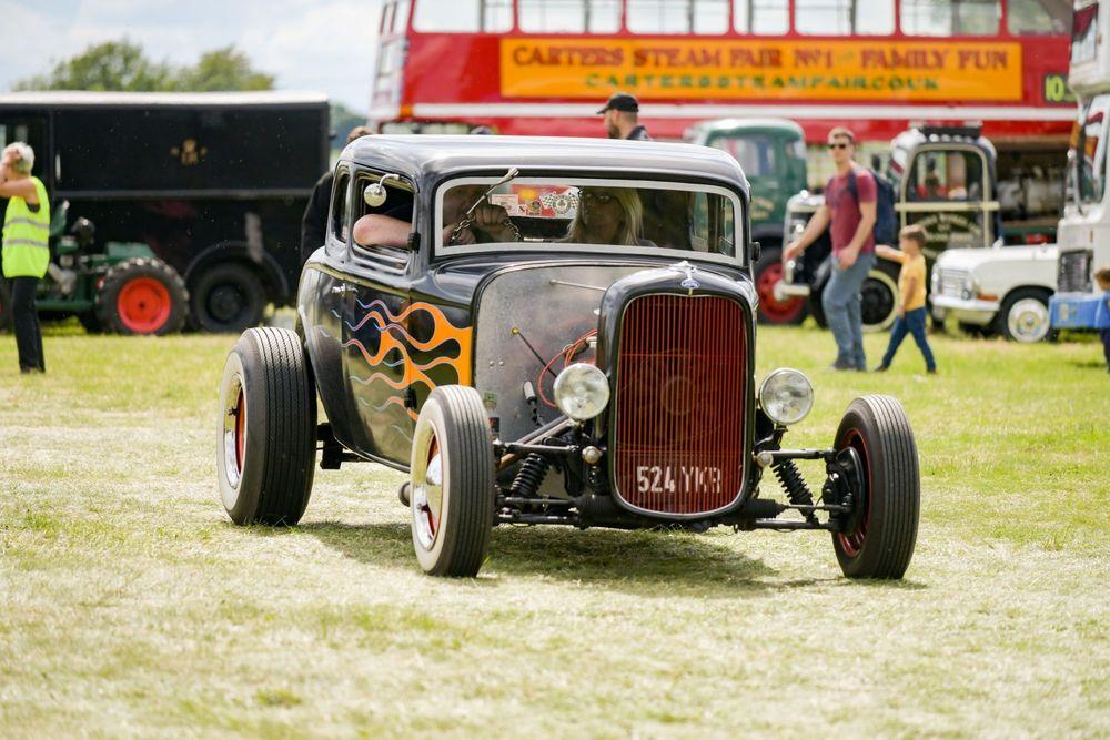 Black hot rod with flames parked in grass at car event.