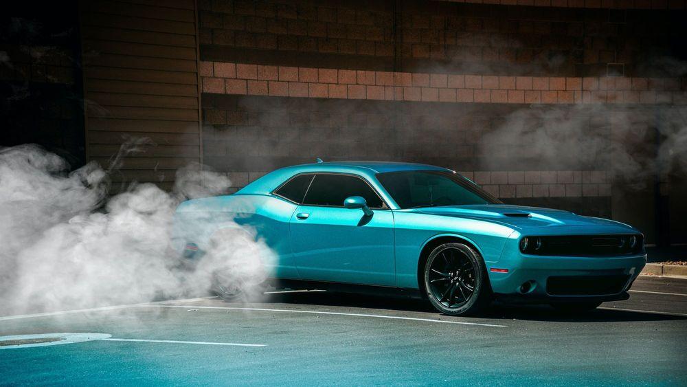 Blue Dodge Challenger in parking spot with smoke around it.