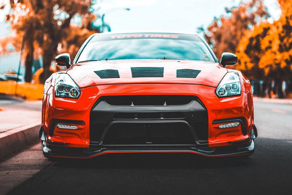 Front of orange custom car parked on asphalt road.