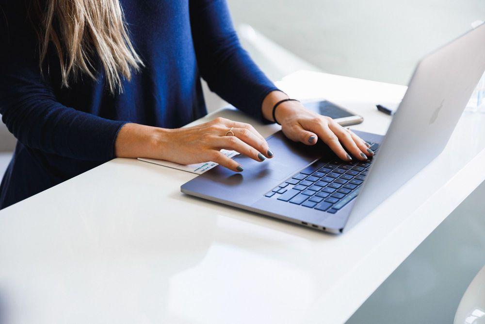 Woman at white desk using a laptop.