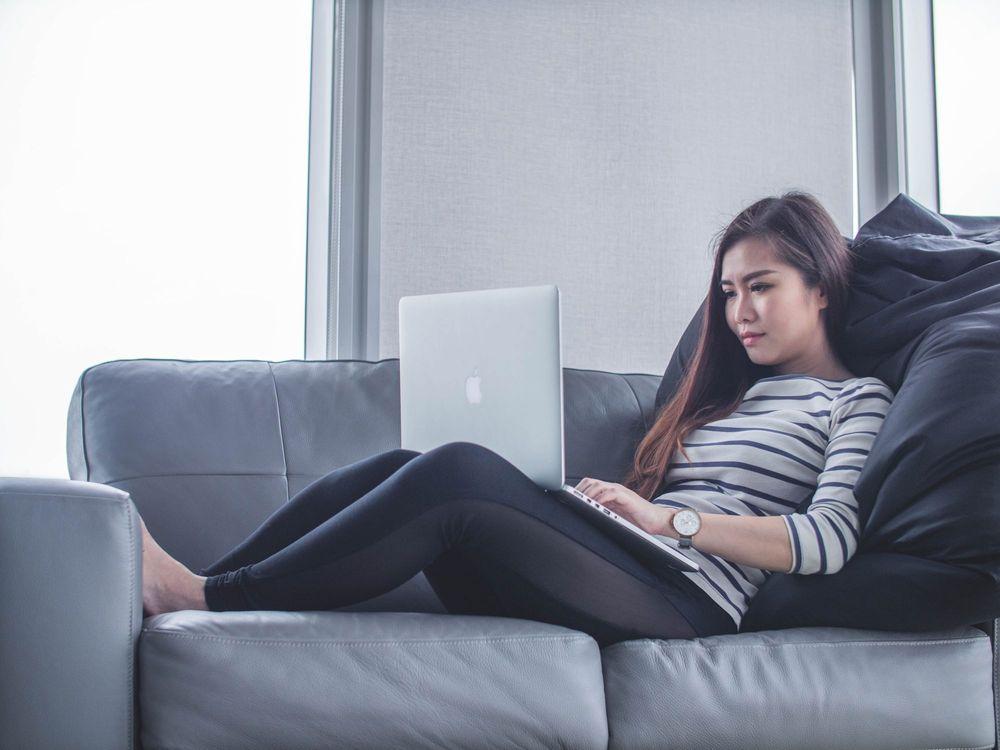 Woman on gray leather couch using laptop.