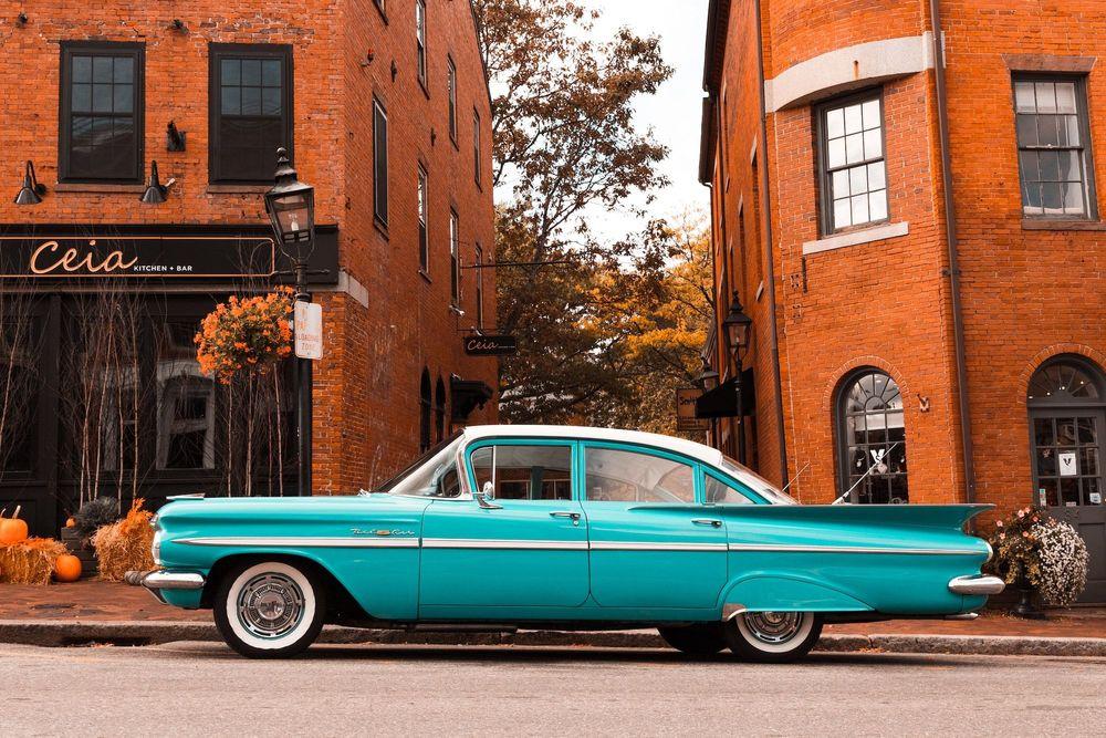 Teal Classic Car parked on the street in front of 2 brick buildings