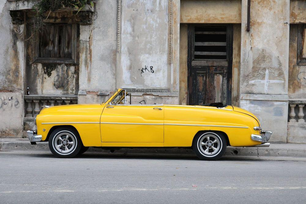 Yellow classic convertible car in front of old cement building