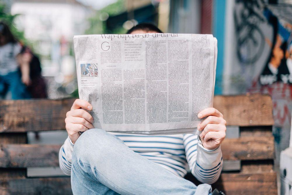 Man reading newspaper on old wooden bench