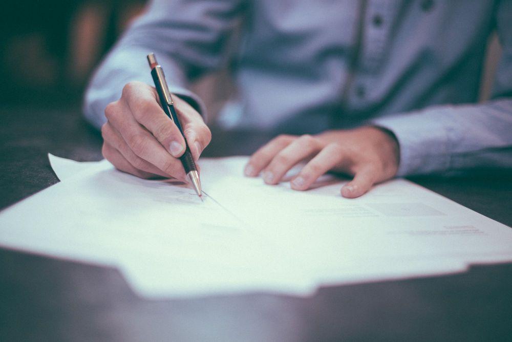 Man in blue dress shirt signing documents with pen.